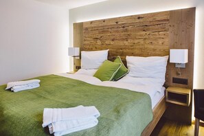 Habitación de hotel con cabecera de madera, colcha verde, almohadas blancas y dos lámparas de noche.