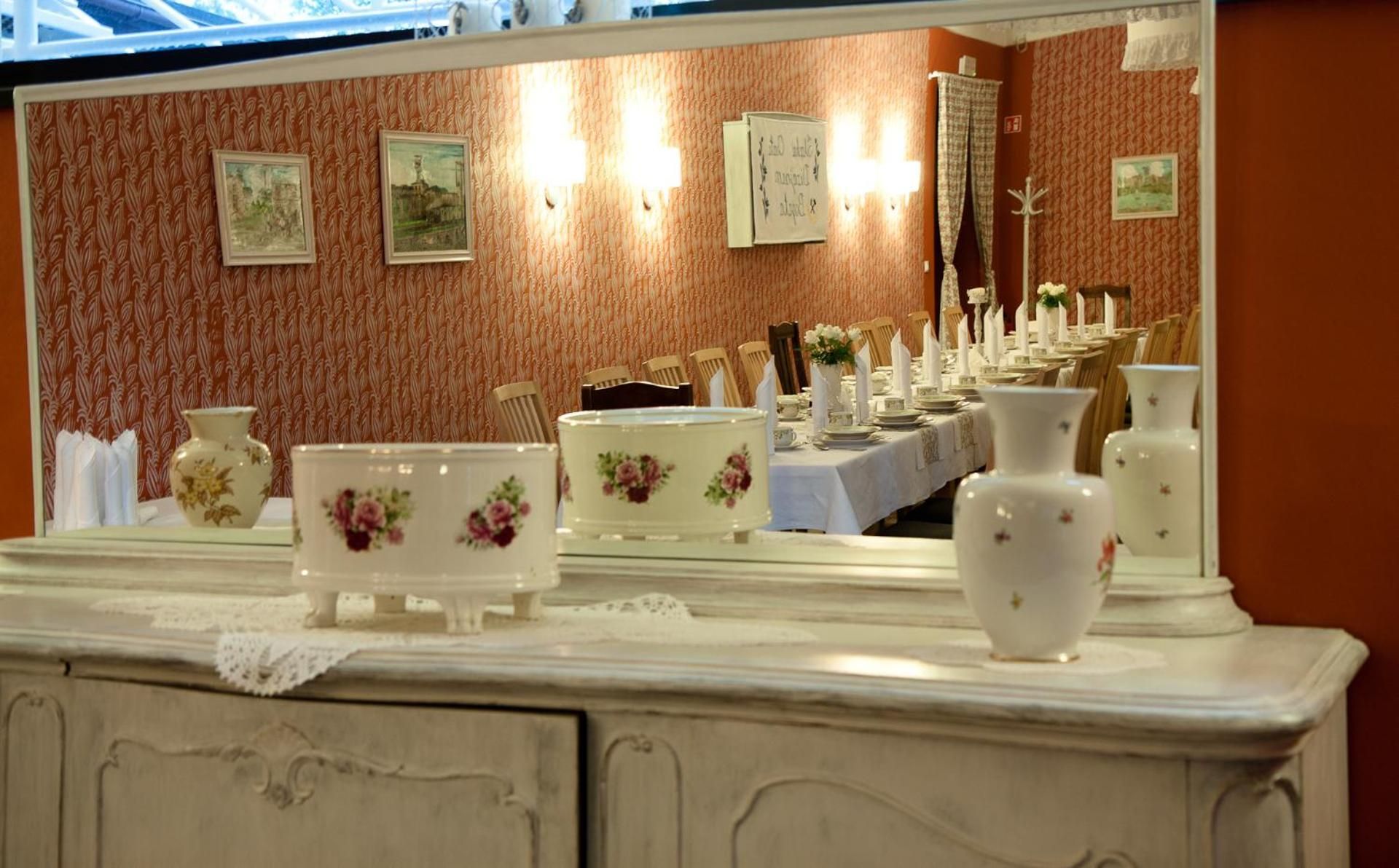 A dining area with a long table set for a meal, a mirror reflecting the room, and a decorative vase on the counter.