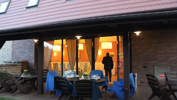 An outdoor seating area with tables and chairs, a covered entrance, and a brick wall.