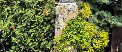 A stone pillar with a sculpture, surrounded by lush greenery and flowering plants.