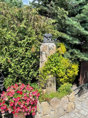 A stone pillar with a sculpture, surrounded by lush greenery and flowering plants. - Karczma Michelle (Olawa)