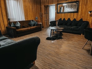 A room with a brown sofa, a black sofa, a round table, and a wooden floor.