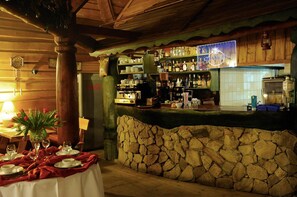 A rustic bar area with a stone wall, wooden shelves stocked with bottles, and a Coca-Cola refrigerator. - Karczma Michelle (Olawa)