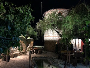 A stone structure with a circular opening, surrounded by greenery and outdoor seating.
