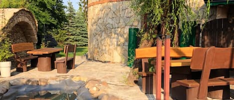 Una estructura de piedra con un banco y una mesa de madera, un pequeño estanque y una cerca de madera.