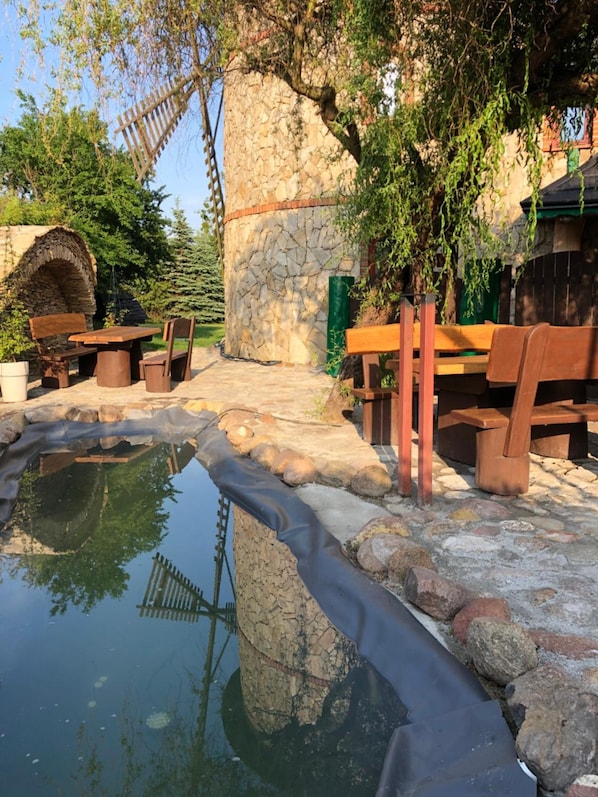 A stone structure with a wooden bench and table, a small pond, and a wooden fence.