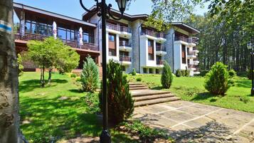A multi-story building with balconies, a stone facade, and a well-maintained garden with a stone pathway leading to the entrance.