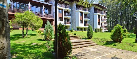 A multi-story building with balconies, a stone facade, and a well-maintained garden with a stone pathway leading to the entrance.