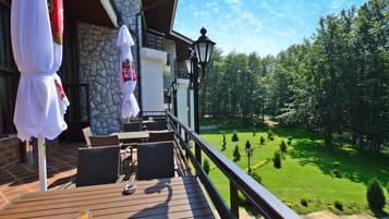 A wooden deck with outdoor furniture, a stone wall, and a view of a green landscape.