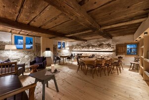 Interior rústico com parede de pedra, móveis de madeira e teto alto.