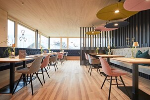 Un comedor moderno con pisos de madera, varias opciones de asientos e iluminación colgante.