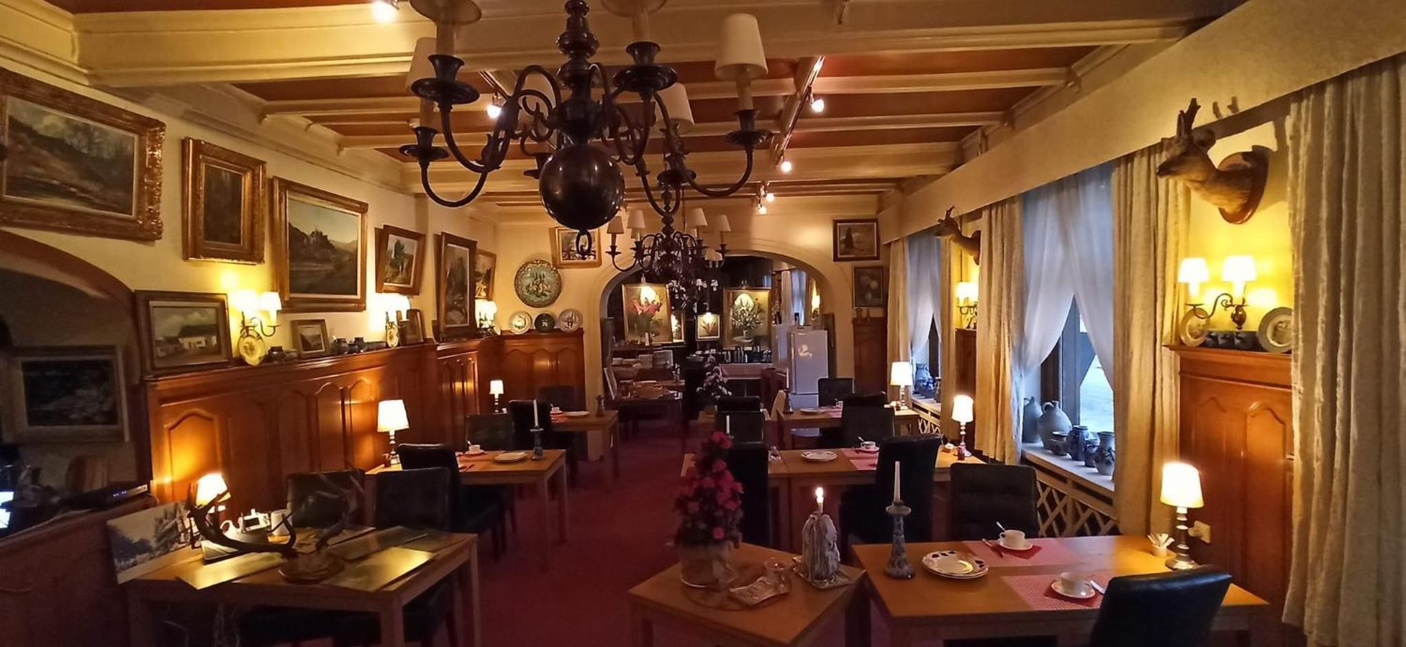 Een restaurantgedeelte in een hotel, met meerdere tafels, kroonluchters en wandlampen.