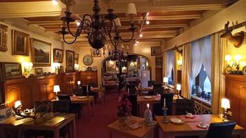 Een restaurantgedeelte in een hotel, met meerdere tafels, kroonluchters en wandlampen.