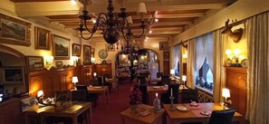 A hotel dining area with multiple tables, chandeliers, and wall-mounted lamps. - Hotel Le Chalet (La Roche-en-Ardenne)