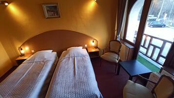 Een hotelkamer met twee bedden, een stoel, een kleine tafel en een raam met uitzicht op de straat.