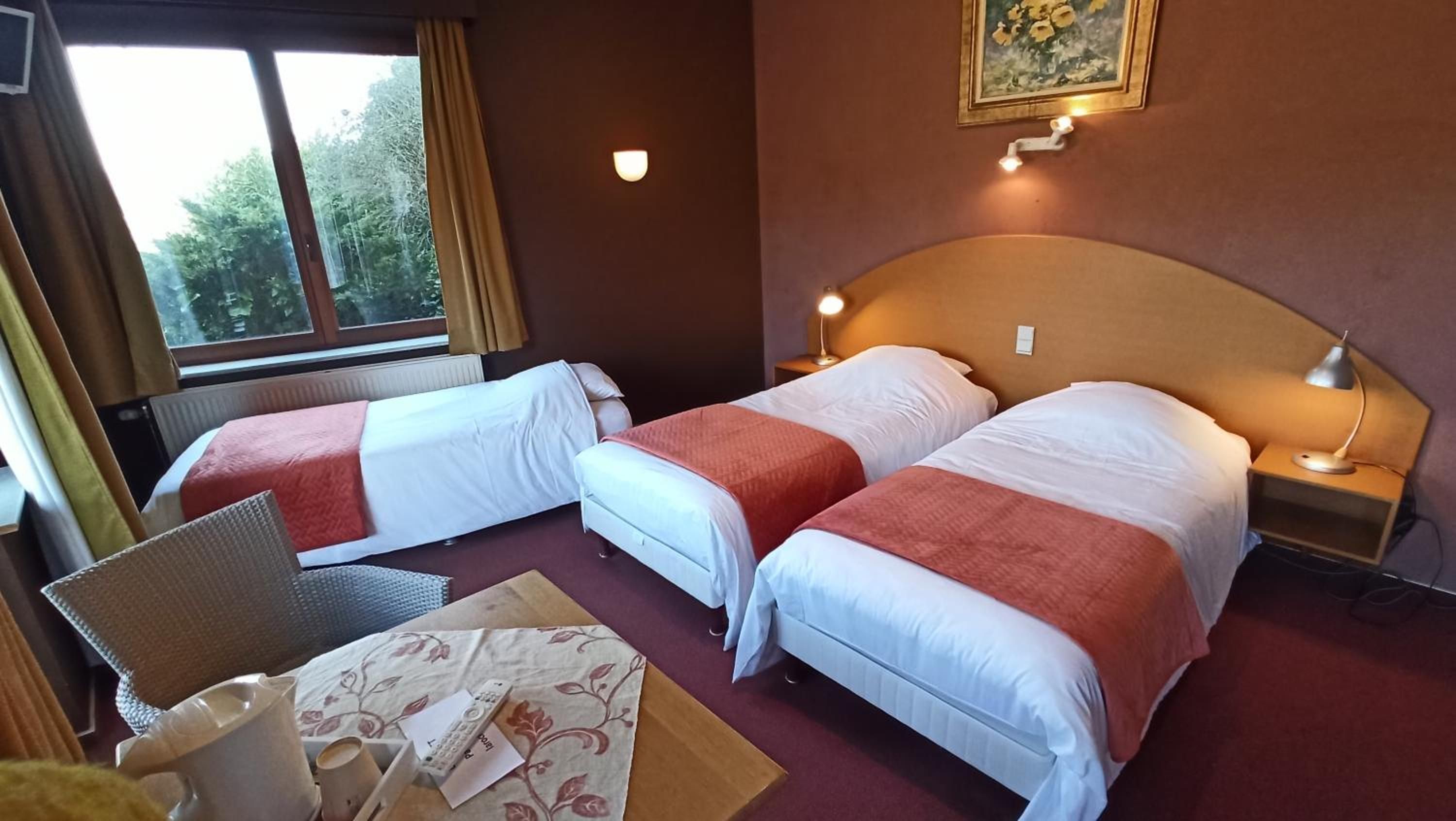 Een hotelkamer met twee bedden, een bureau, een stoel, een lamp en een schilderij aan de muur.