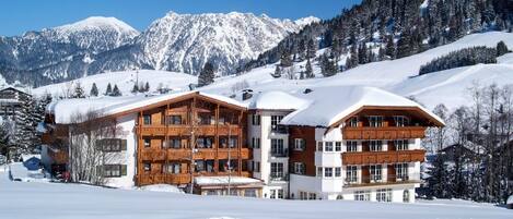A multi-story wooden building with balconies, set against a snowy mountain backdrop.