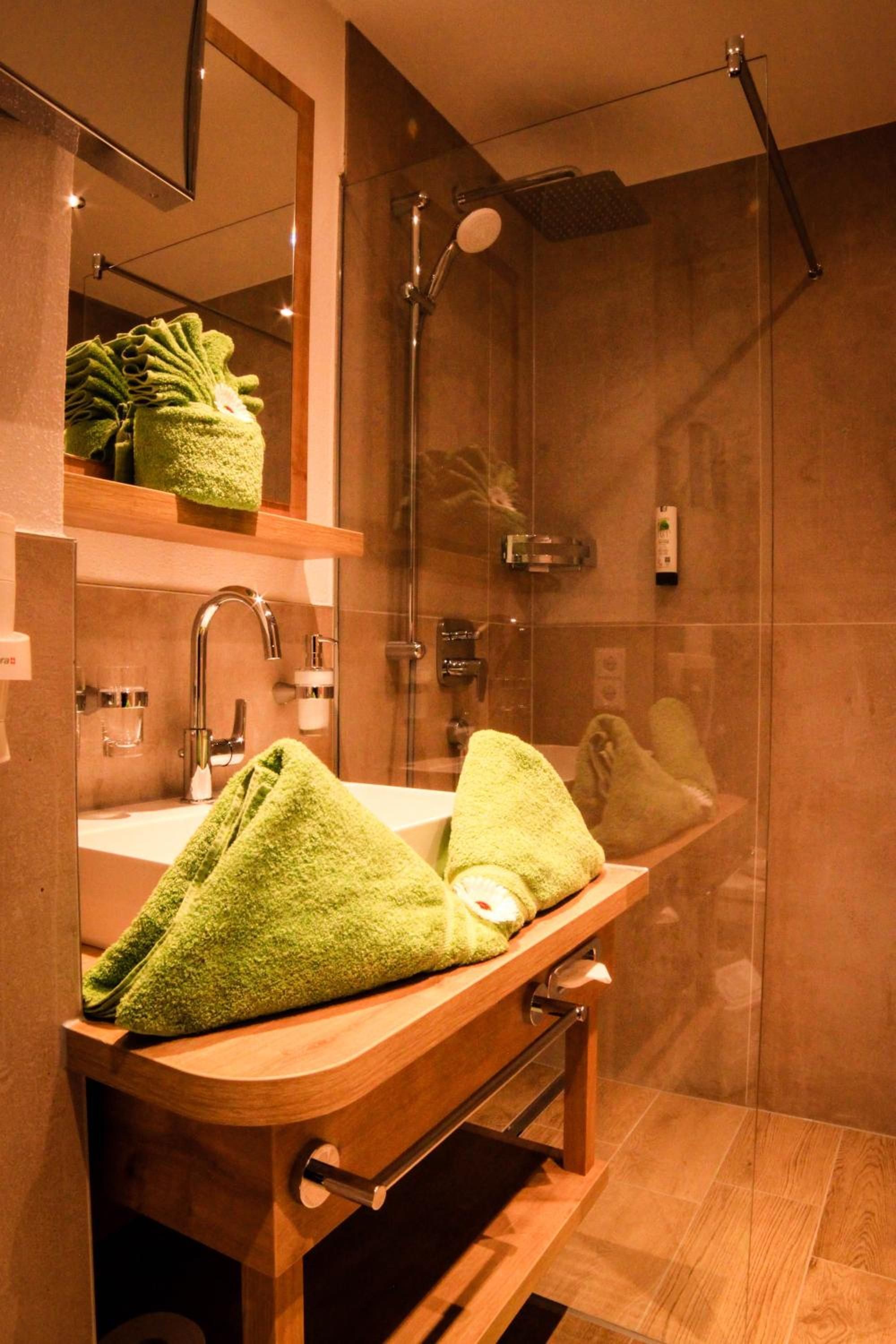 Ein modernes Badezimmer mit einem Holzkosmetikschrank, einem Spiegel, einer Dusche und einem Handtuchhalter.
