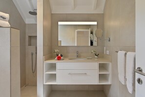 Un baño moderno con tocador blanco, espejo, ducha y perchero.