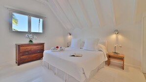 Un dormitorio con una cama grande, un aparador de madera, una mesita de noche y una ventana con vistas a palmeras.
