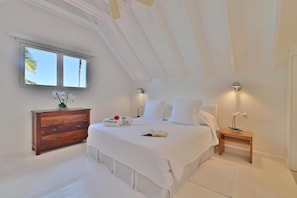 Un dormitorio con una cama grande, un aparador de madera, una mesita de noche y una ventana con vistas a palmeras.
