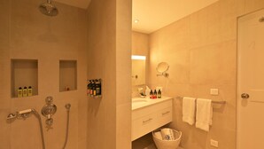 Un baño con ducha, lavamanos, espejo y toallero.