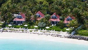 Propiedad frente al mar con varias casas, una playa de arena y palmeras.