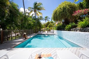 A swimming pool with a wooden deck, surrounded by palm trees and tropical plants.