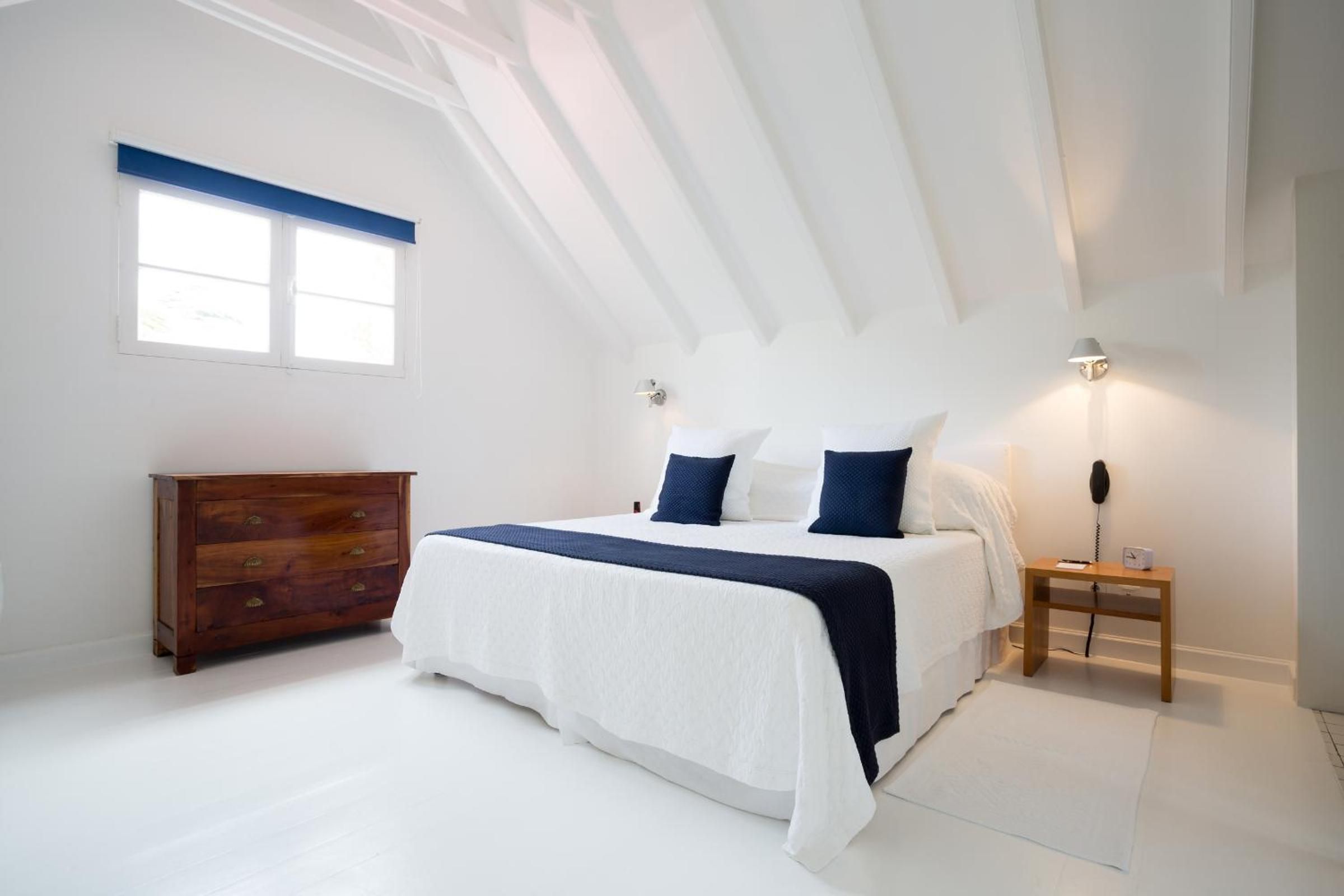 Et soveværelse med seng, kommode, sengebord, lampe og et vindue.