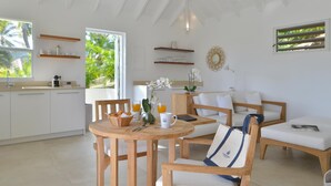 Una cocina moderna con armarios blancos, un comedor con sillas de madera y una mesa redonda, y vistas a palmeras a través del ventanal.