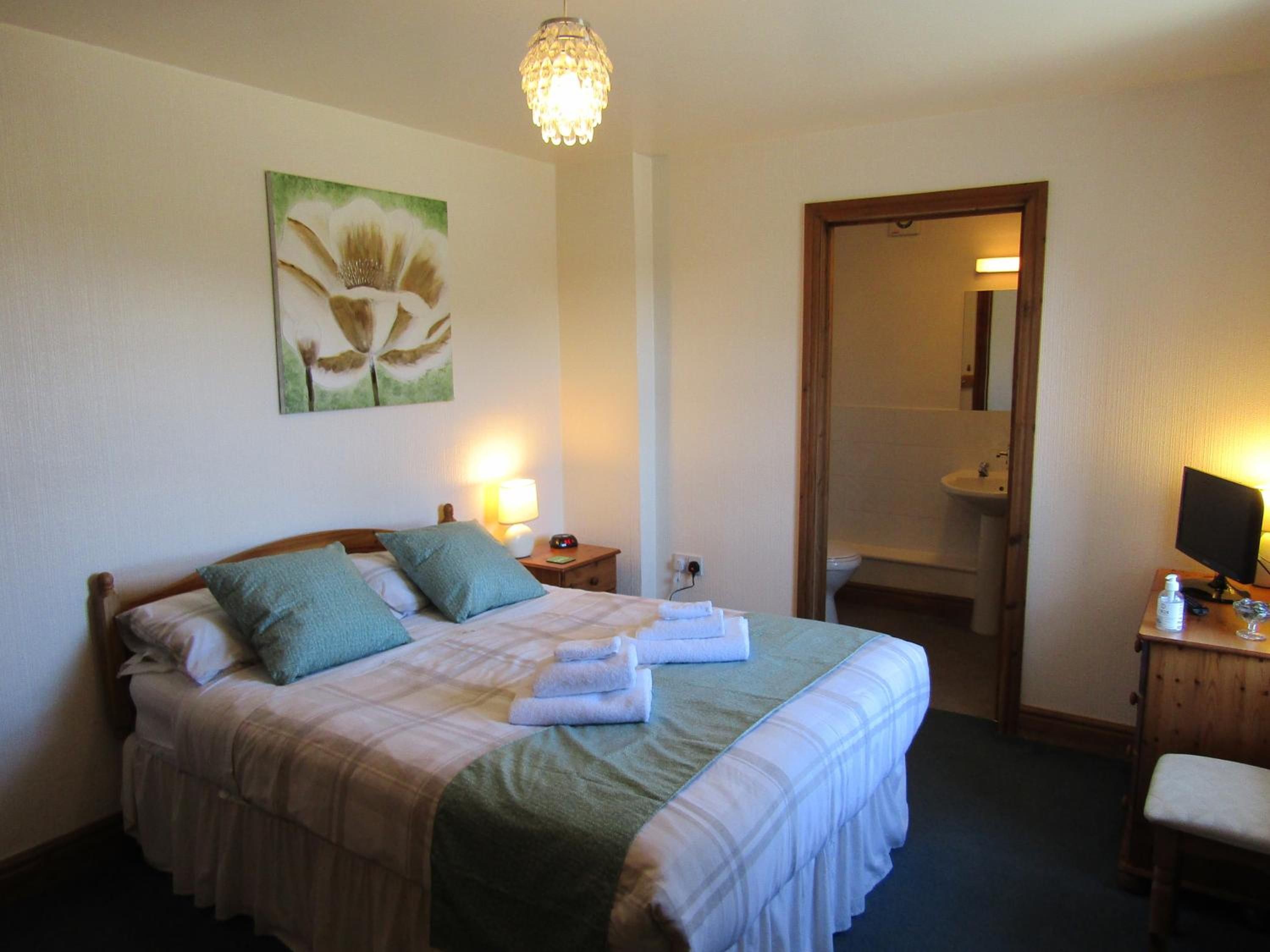 Habitación de hotel con una cama, una mesita de noche con lámpara, un cuadro en la pared y un baño visible a través de una puerta abierta.