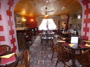 Un espace repas avec des tables et des chaises en bois, une moquette à motifs et un plafond en bois agrémenté d’un lustre.
