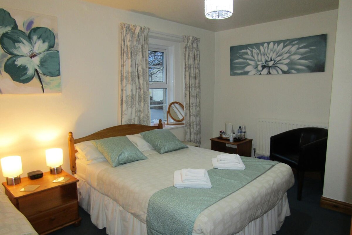 Une chambre d’hôtel avec un lit, des lampes de chevet, un bureau, une chaise et des œuvres d’art accrochées aux murs.