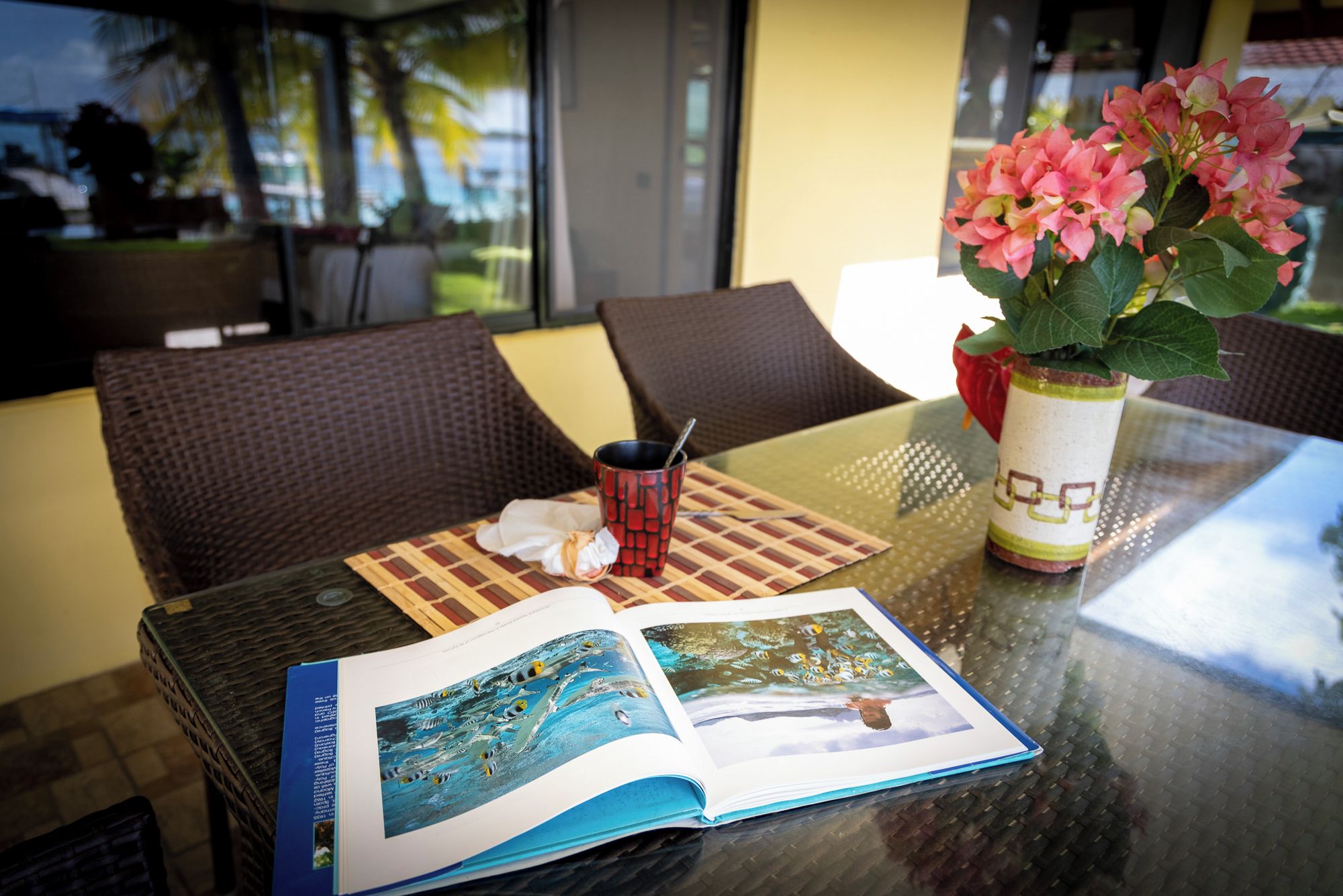 A table with a book, a red mug, and a potted plant with pink flowers.