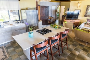 A modern kitchen with a central island, bar stools, a refrigerator, and a dining area with a television.