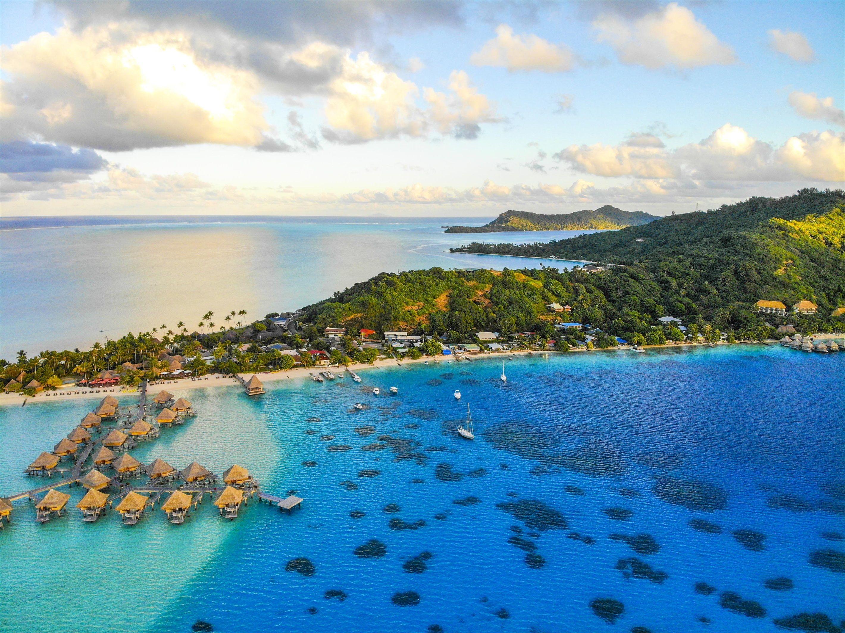 An aerial view of a coastal resort with overwater bungalows, clear blue waters, and a beach.