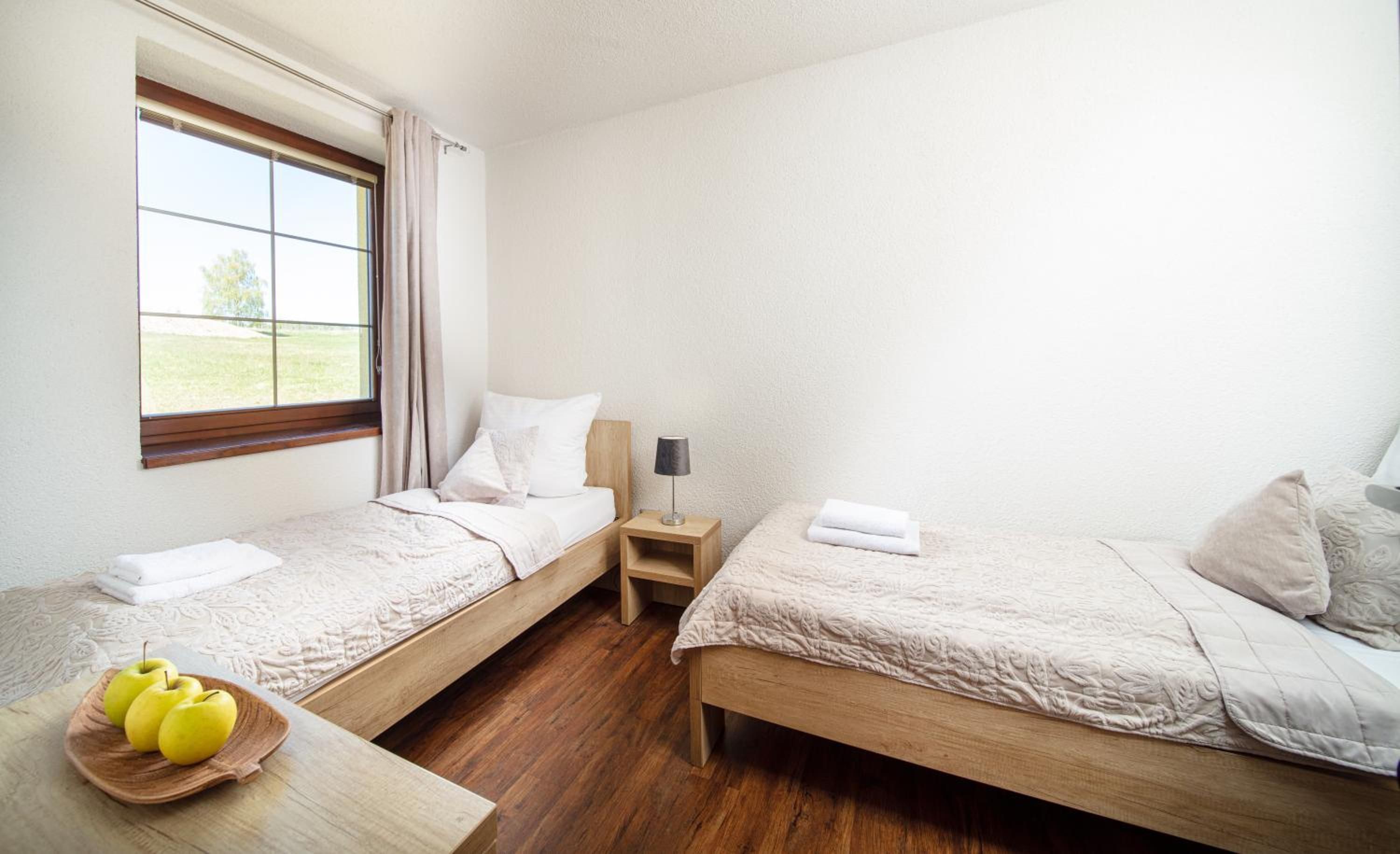 Habitación de hotel con dos camas individuales, una mesita de noche de madera, una lámpara y una pequeña mesa con manzanas.