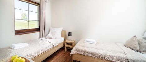 Habitación de hotel con dos camas individuales, una mesita de noche de madera, una lámpara y una pequeña mesa con manzanas.