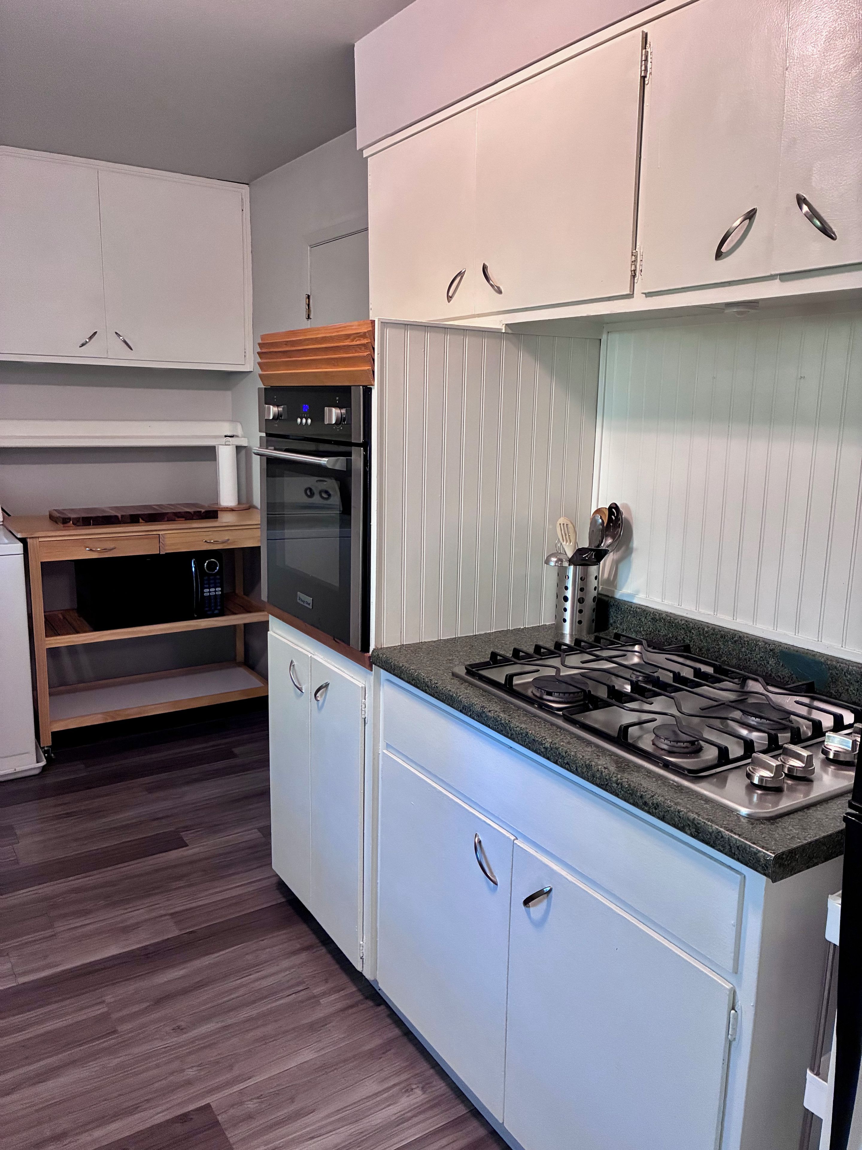 A compact kitchen with white cabinets, a built-in oven, a gas stove, and a wooden countertop.