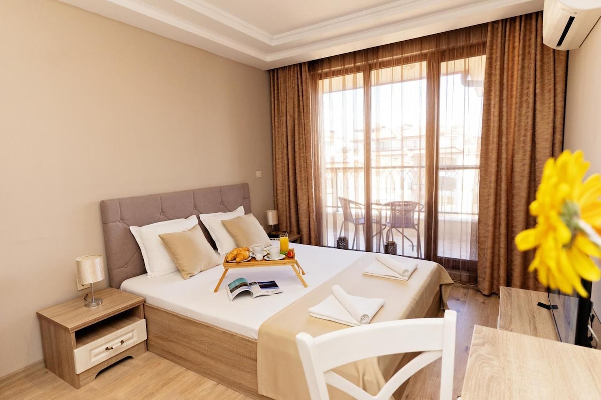 A hotel room with a bed, bedside table, and a dining area with a chair and table.