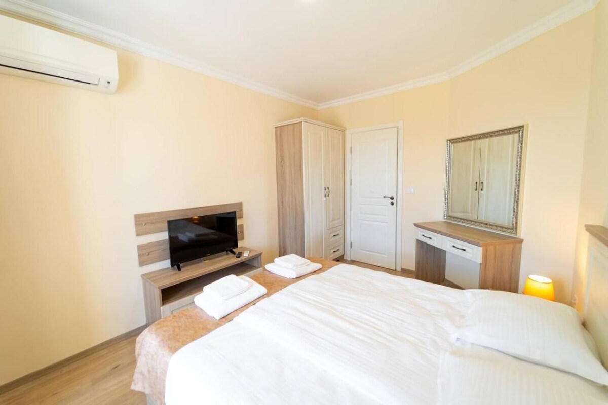A hotel room with a bed, a TV, a wardrobe, a desk, and a mirror.