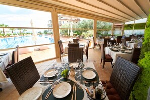 A restaurant with outdoor seating overlooking a swimming pool and a view of buildings. - Burgas Beach Resort Apartments (Burgas)