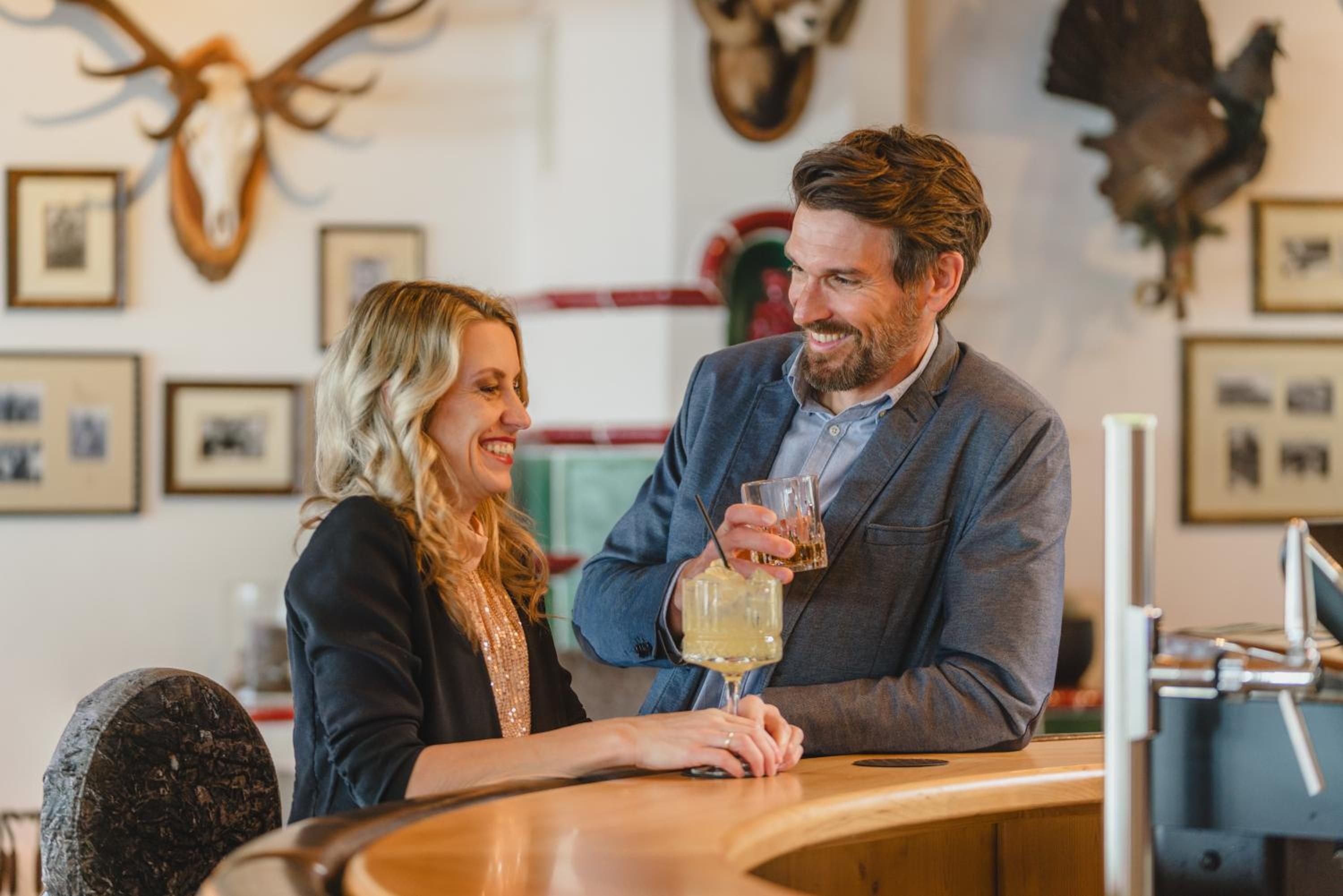 A couple seated at a bar with a rustic interior, including antlers on the wall and framed pictures.