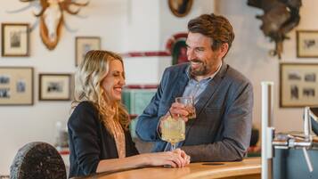 A couple seated at a bar with a rustic interior, including antlers on the wall and framed pictures.