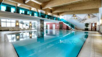 An indoor swimming pool with a clear view of the pool area, a staircase leading to an upper level, and a red wall with a door.
