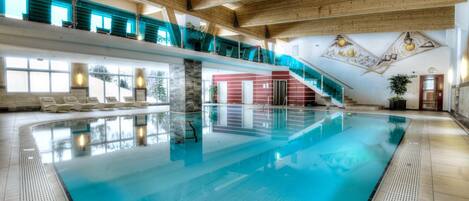 Una piscina interior con vista despejada al área de la piscina, una escalera que lleva a un nivel superior y una pared roja con una puerta.