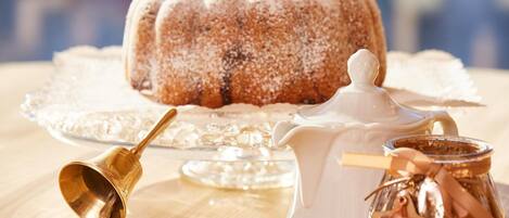 Un pastel bundt sobre un soporte de vidrio, una jarrón blanco y un frasco con tapa en forma de estrella sobre una mesa de madera.