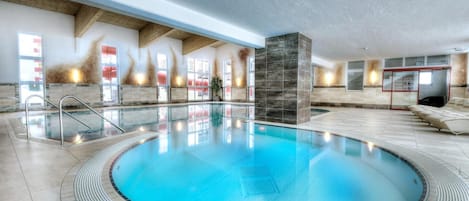 A large indoor swimming pool with a circular design, surrounded by a tiled deck and a lounge area with seating.