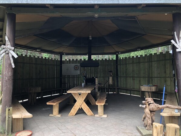 An outdoor pavilion with a table and benches, surrounded by a wooden fence.