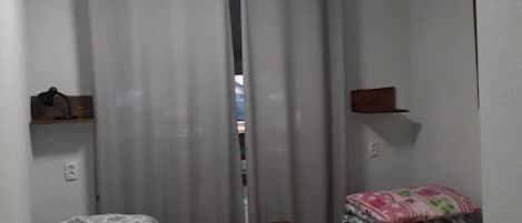 Ein kleines, kompaktes Zimmer mit zwei Einzelbetten, einem kleinen Tisch und einem Regal.